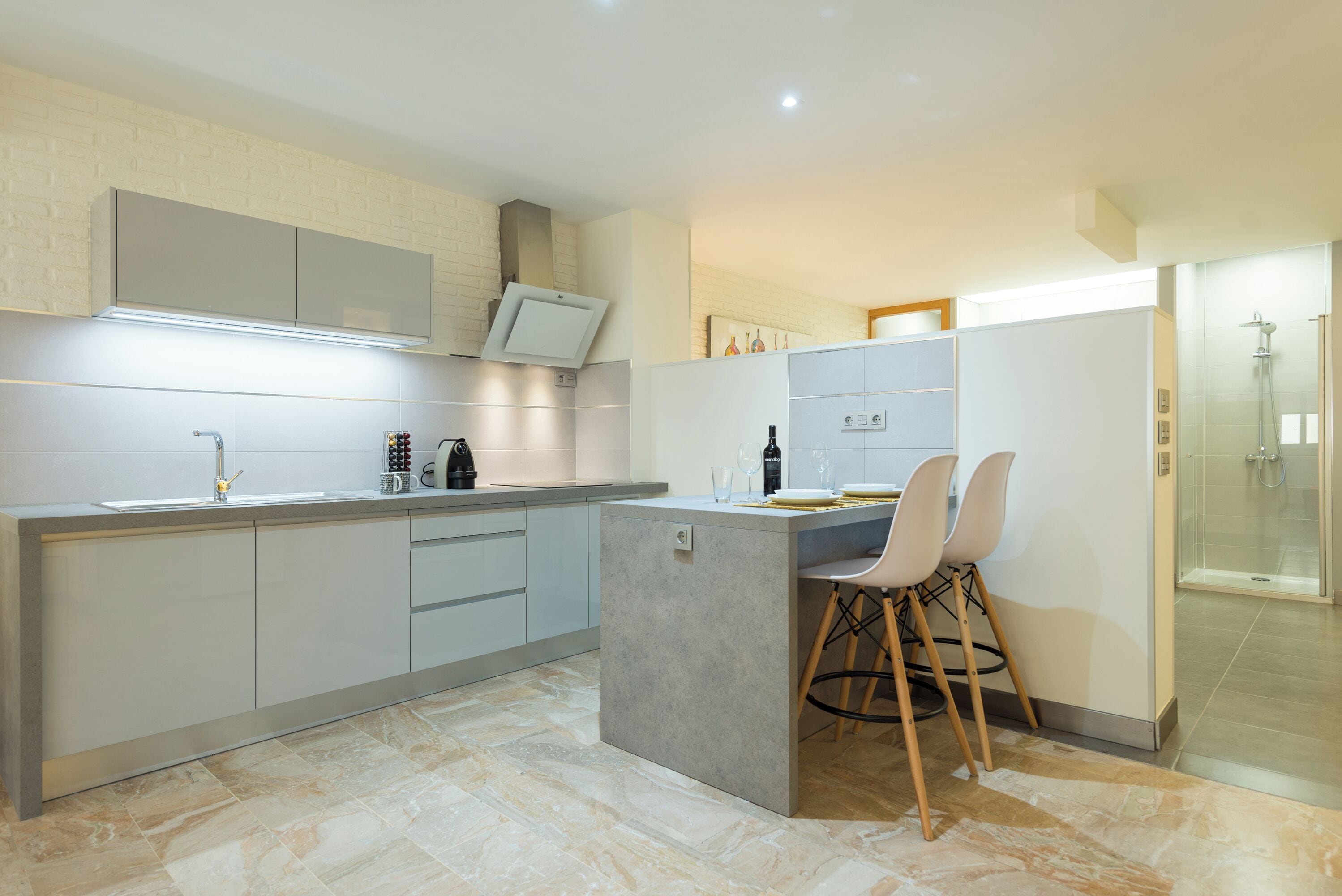 A modern kitchen with a built-in island, a dining area with bar stools, and a glass-enclosed shower.
