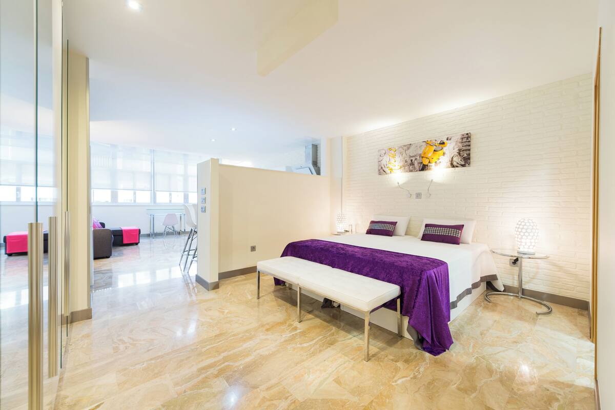 A modern hotel room with a bed, bench, and a view of the city.
