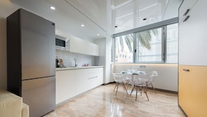 A modern kitchen with a refrigerator, microwave, and dining area with chairs and a table. - Suites Garden (Las Palmas de Gran Canaria)