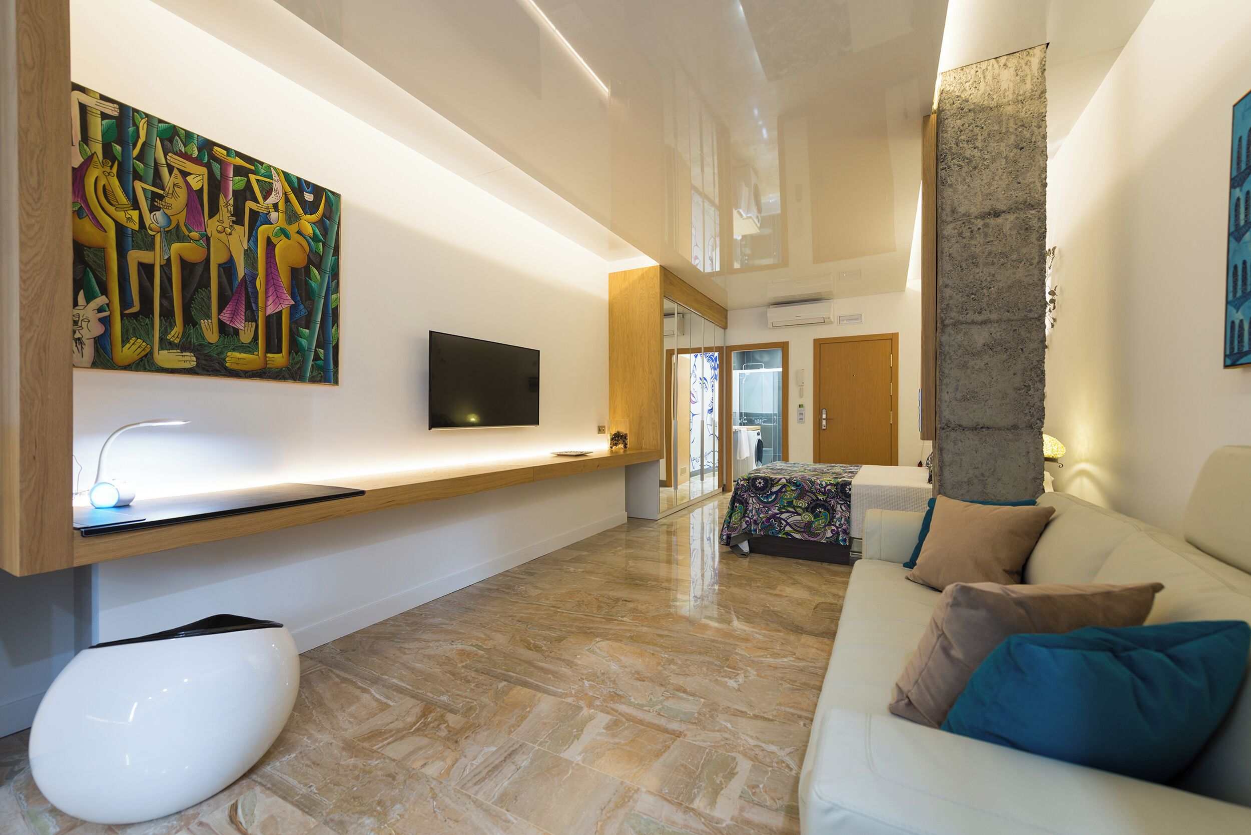 A modern living room with a flat-screen TV, a white sofa, a coffee table, and a large abstract painting on the wall.