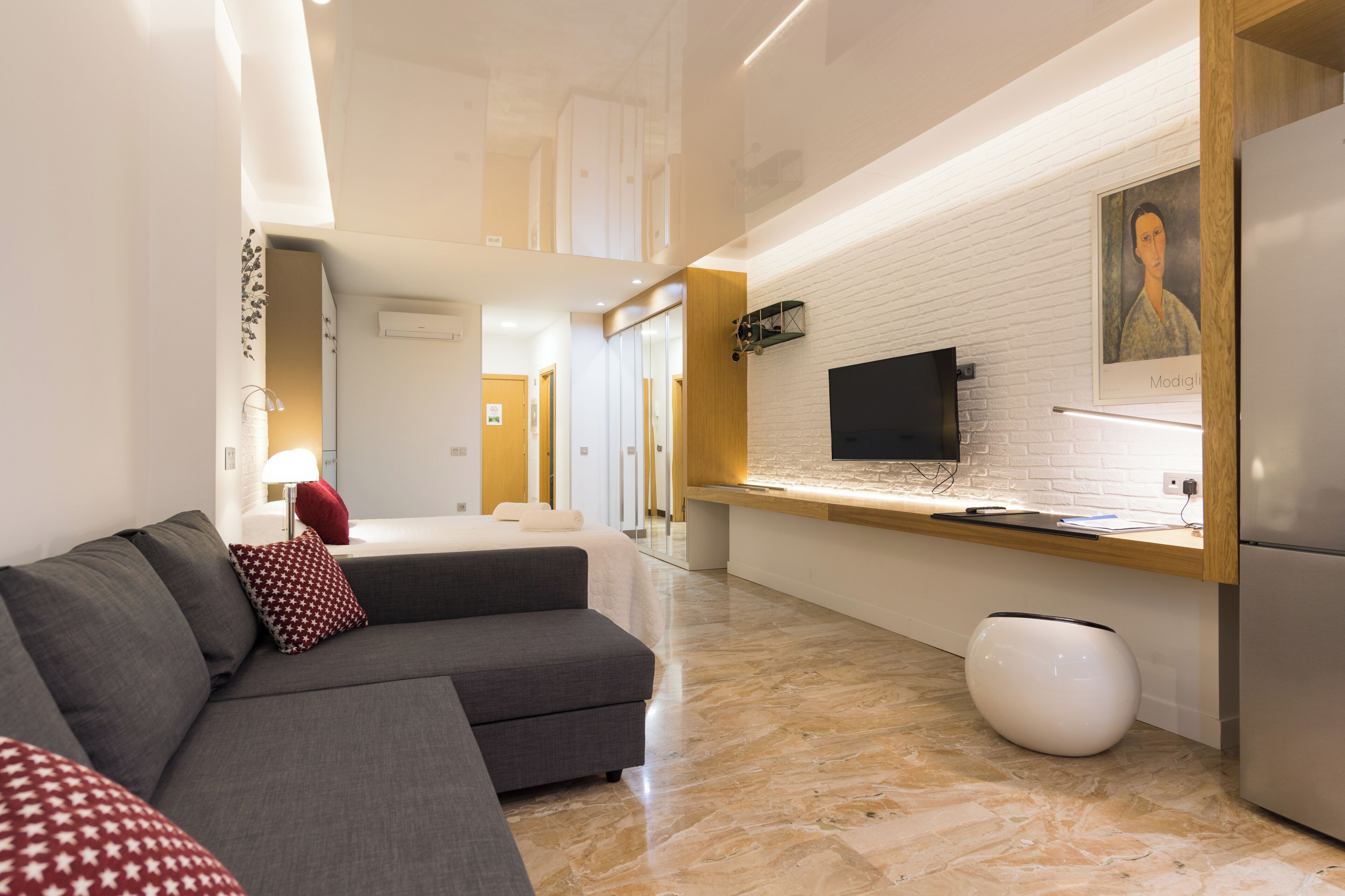 A modern hotel room with a sofa, a flat-screen TV, a white vase, and a wooden counter.