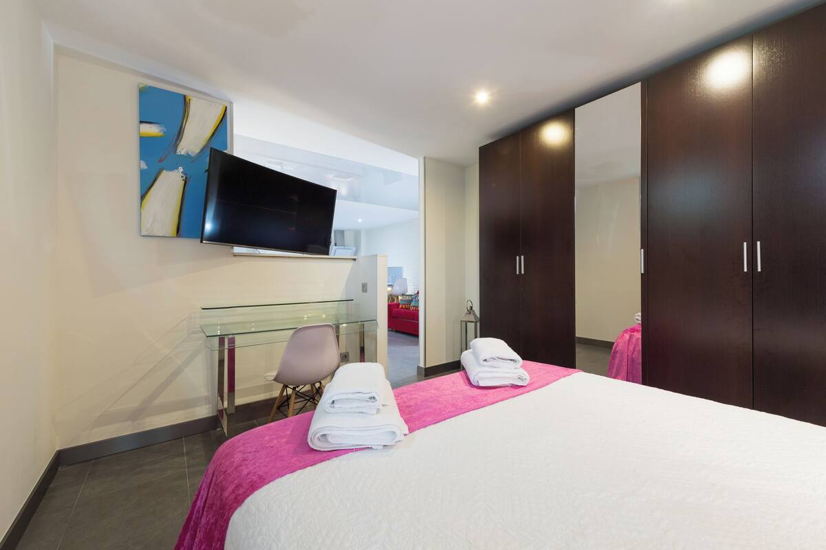 A hotel room with a bed, a TV mounted on the wall, a glass desk, a chair, and a wardrobe.