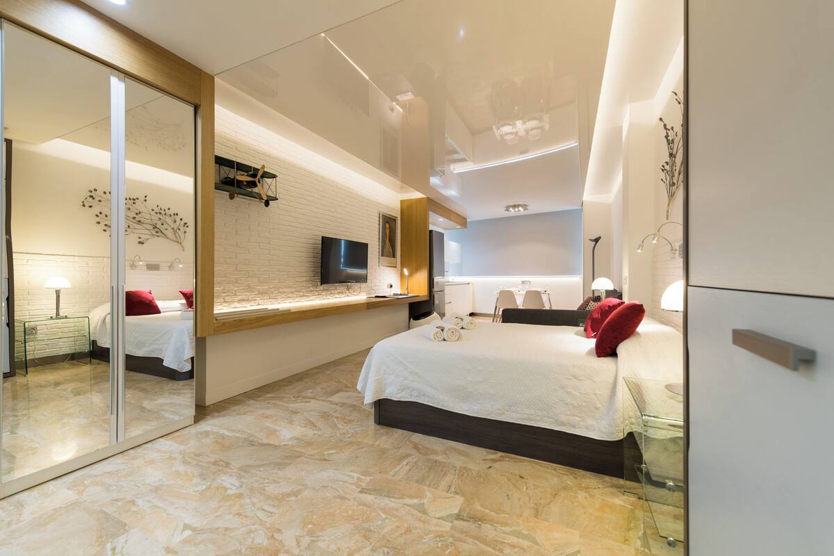 A modern hotel room with a large bed, a TV, a glass shower enclosure, and a mirror.