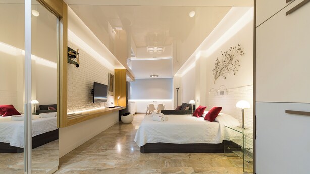 A modern hotel room with a large bed, a TV, a desk, and a mirror. - Suites Garden (Las Palmas de Gran Canaria)