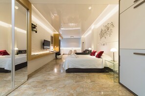 A modern hotel room with a large bed, a TV, a desk, and a mirror. - Suites Garden (Las Palmas de Gran Canaria)