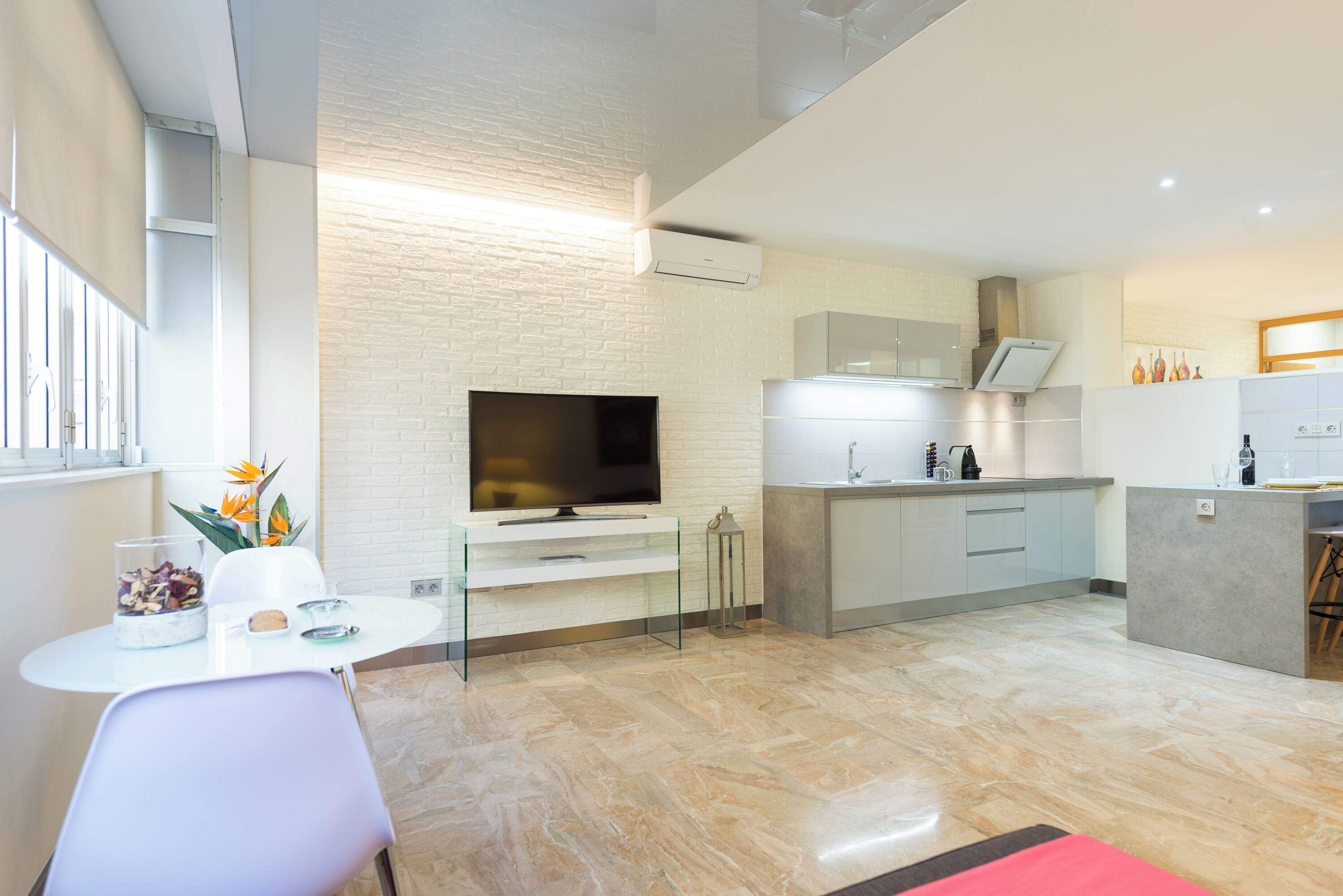 A modern kitchen with a flat-screen TV, a dining area with a table and chairs, and a small side table with decorative items.