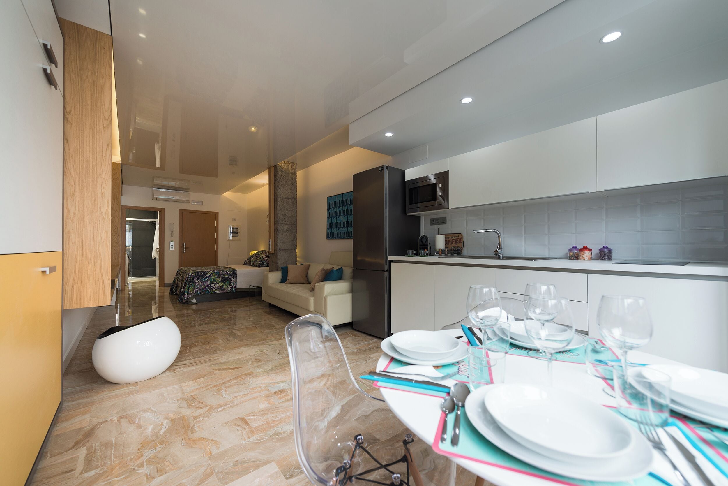 A modern kitchen with a dining area, a sofa, and a clear chair.