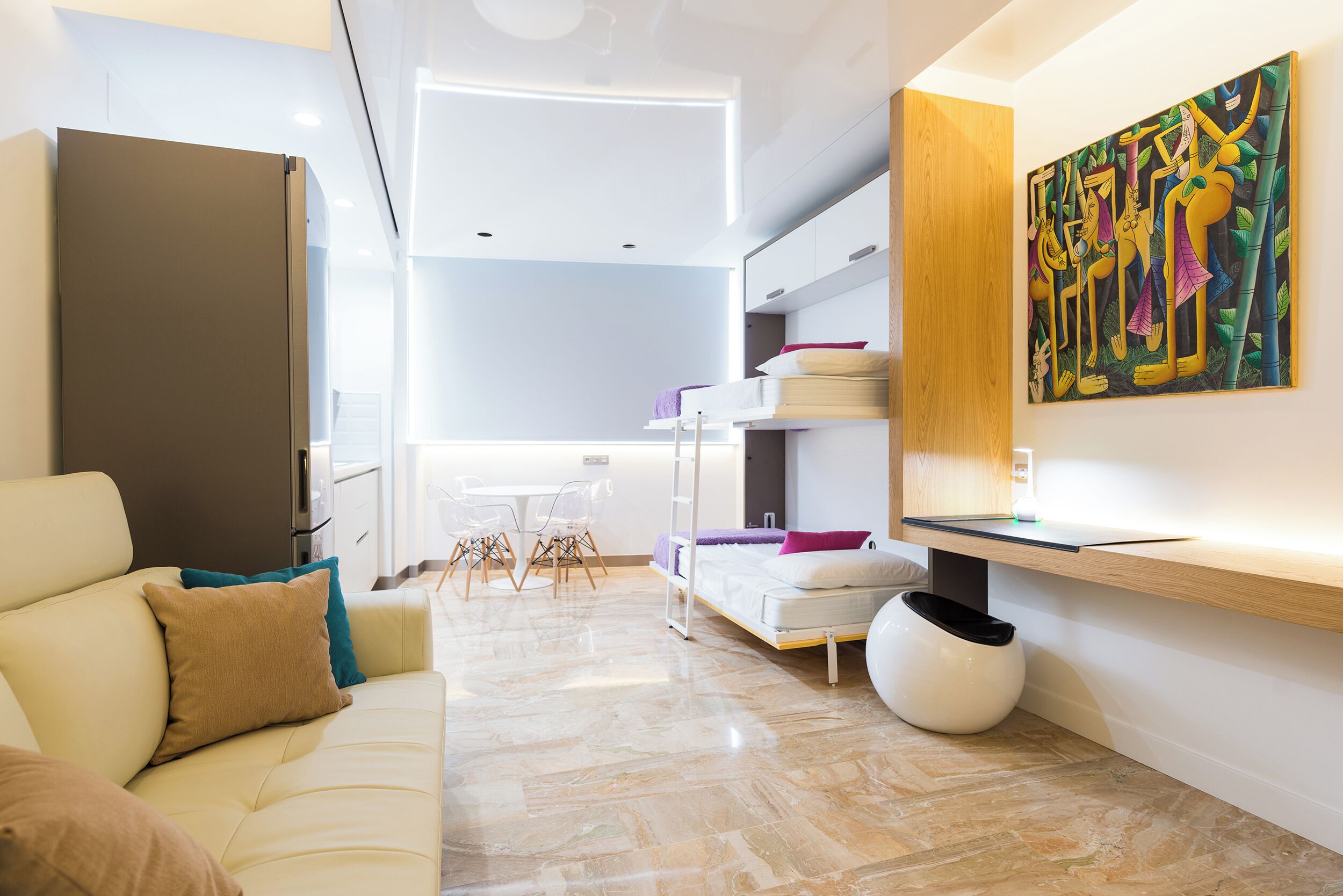 A modern living room with a sofa, a dining table with chairs, a kitchen area, and a painting on the wall.