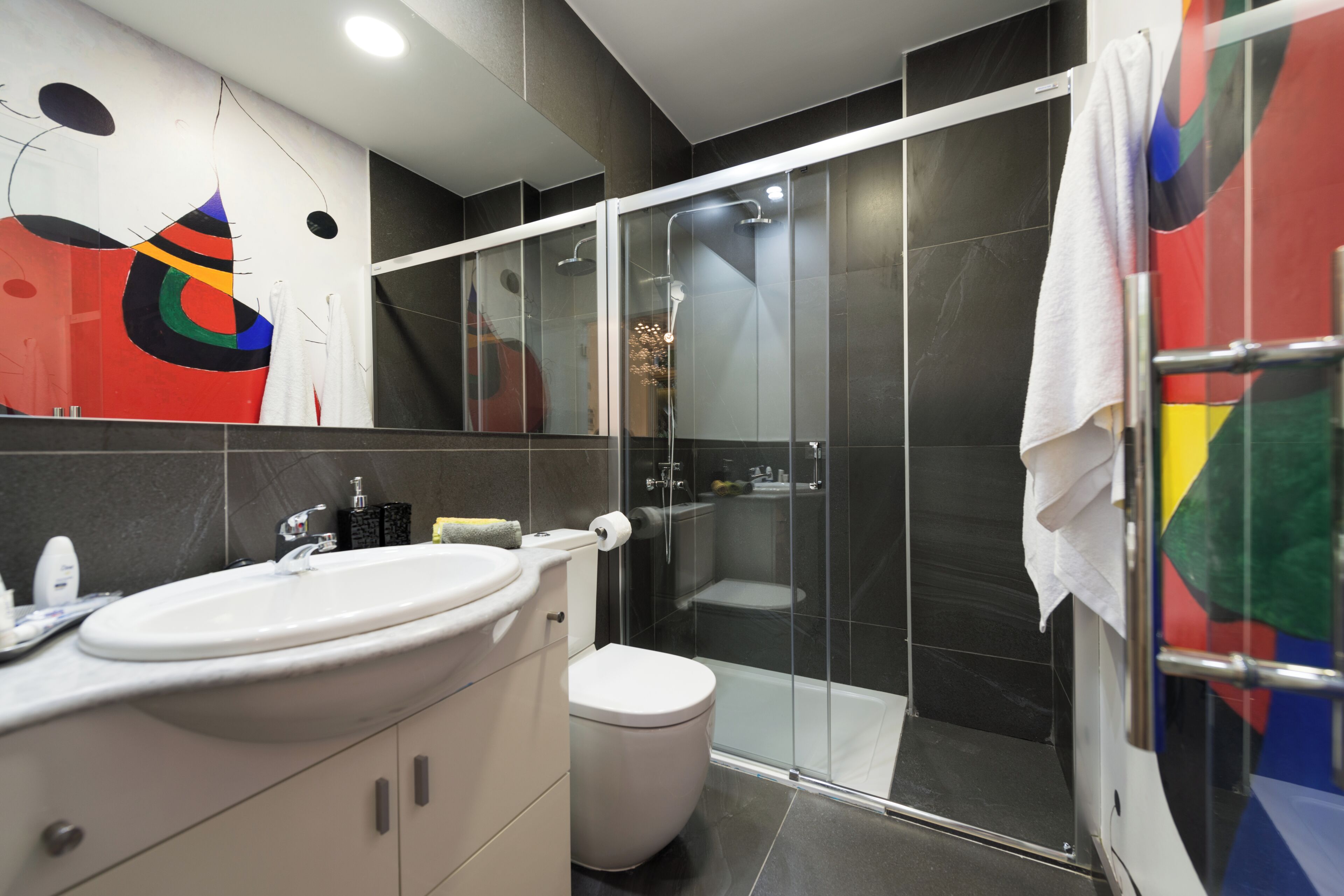 Un bany modern amb dutxa tancada amb vidre, un lavabo blanc i un vàter.