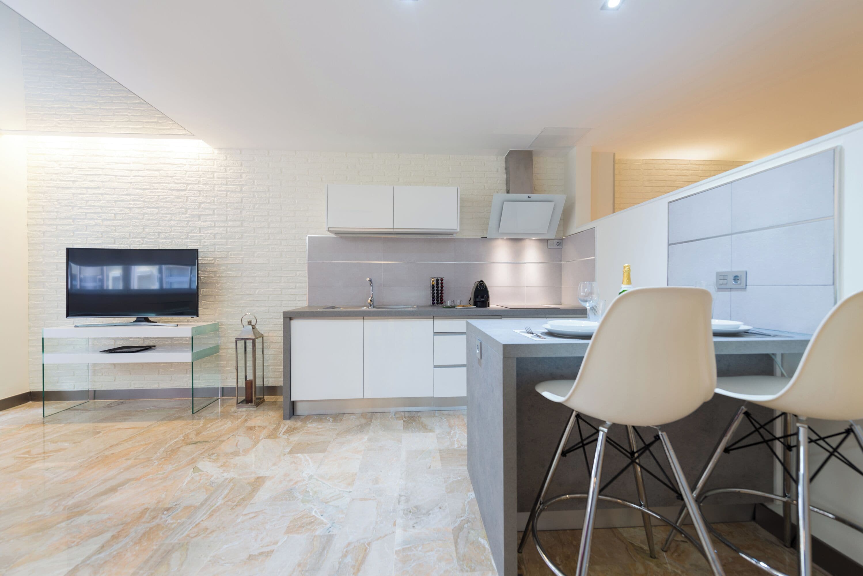 Una cocina moderna con una televisión de pantalla plana, una mesa de comedor de vidrio, sillas blancas y un microondas integrado.