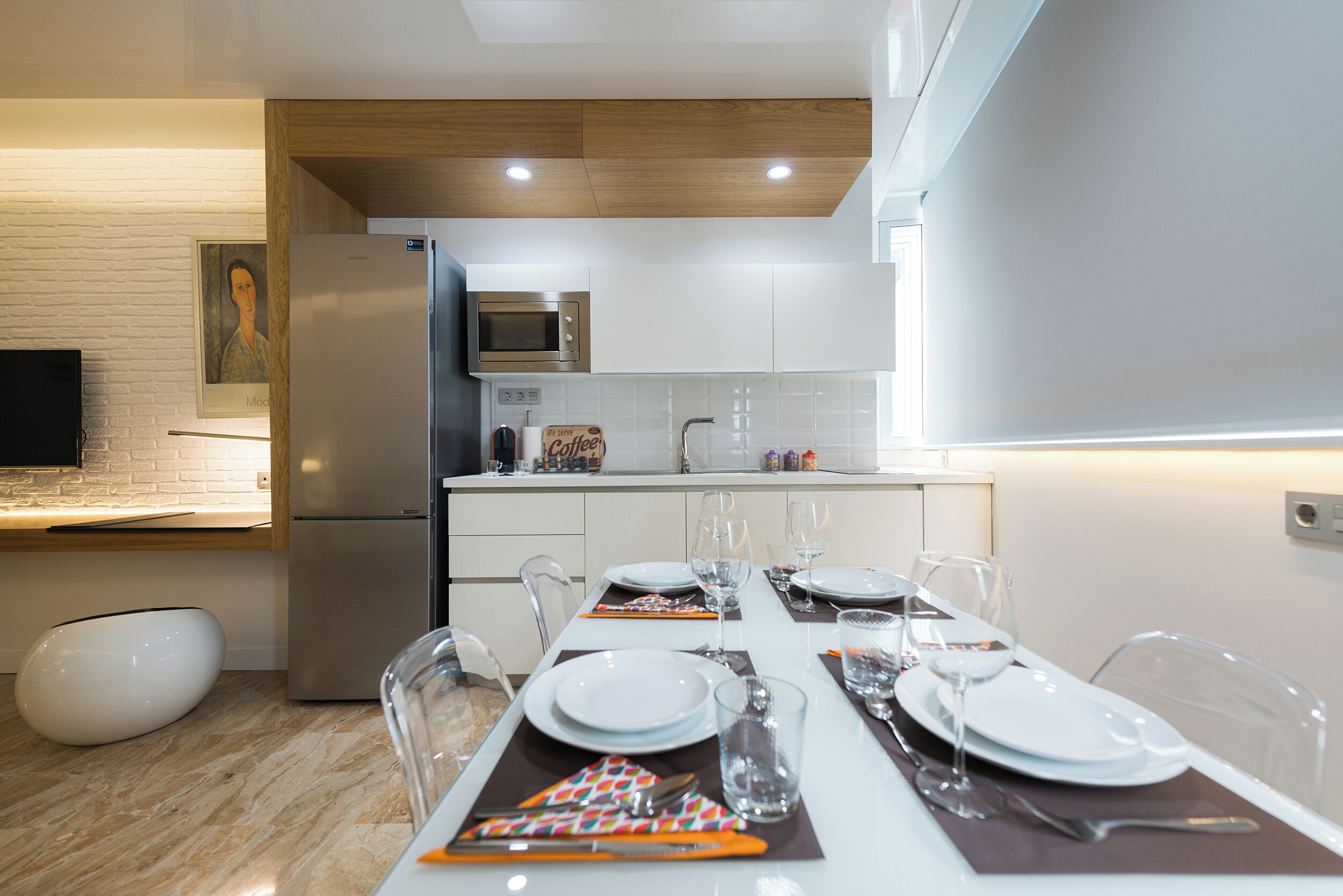 A modern kitchen with a dining area set for a meal, featuring a refrigerator, microwave, and white cabinets.