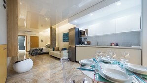 A modern kitchen with a dining area, a sofa, and a clear chair. - Suites Garden (Las Palmas de Gran Canaria)