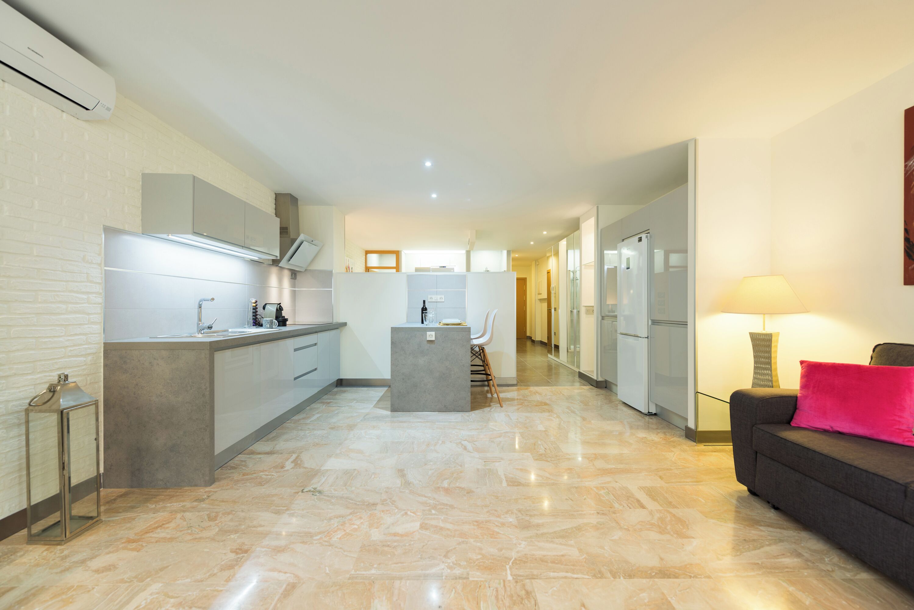 Una cocina moderna con una isla central, un comedor con una silla y un sofá con una lámpara.