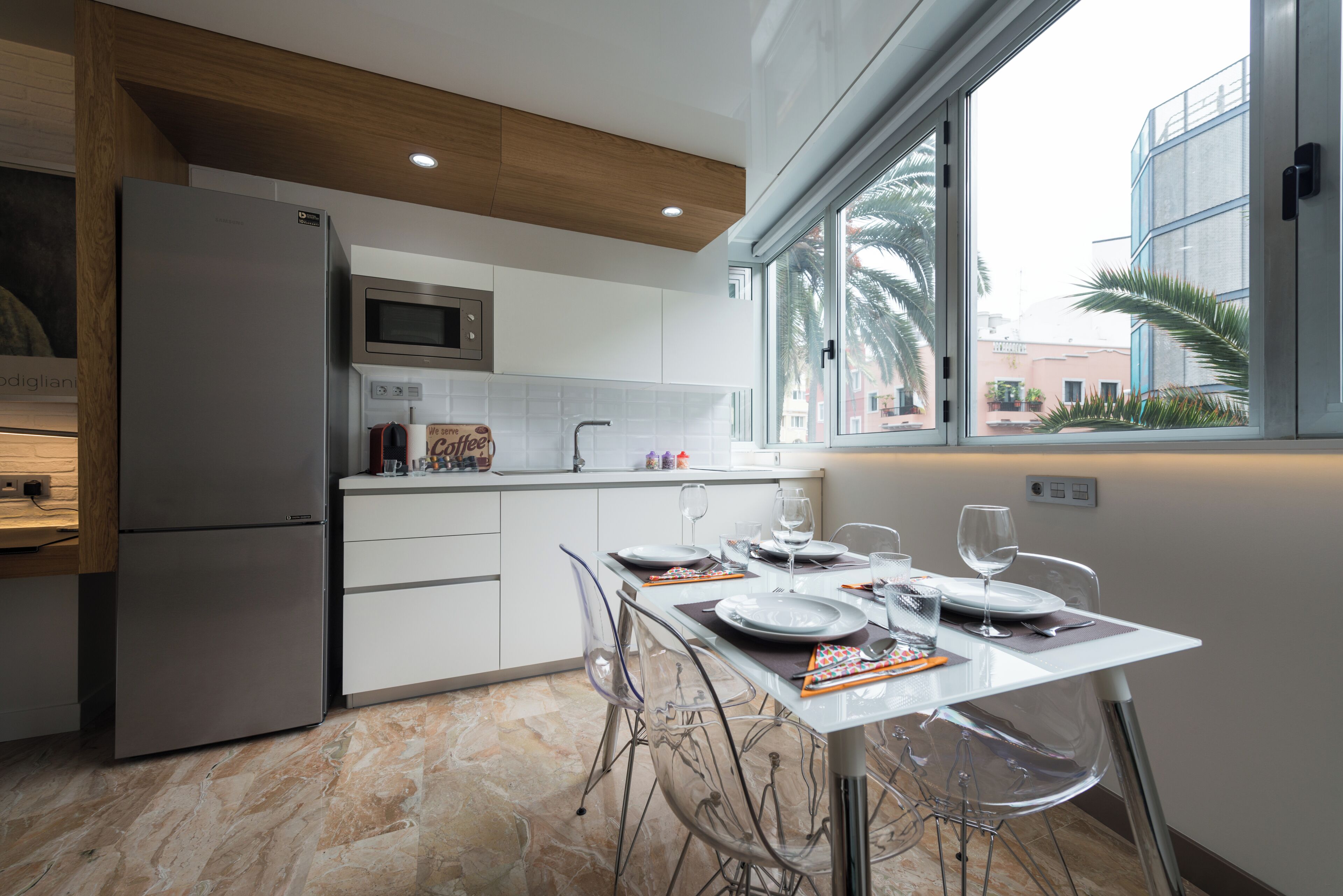 A modern kitchen with a dining area, a refrigerator, microwave, and a window with a view.