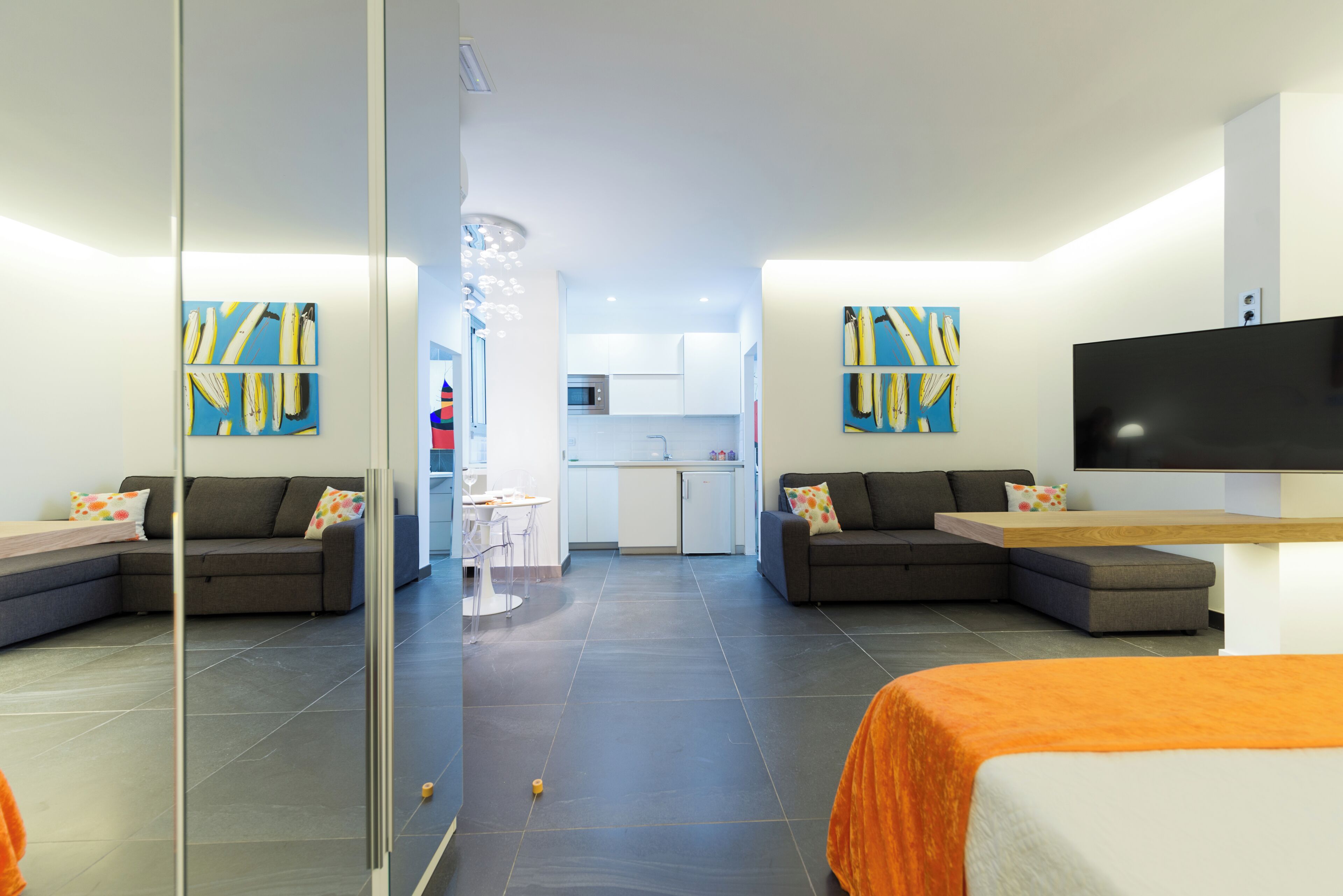 Una habitación de hotel moderna con sofá, cama, televisión y una cocina al fondo.