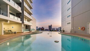 Un edificio moderno con piscina, balcones y un paisaje urbano de fondo.