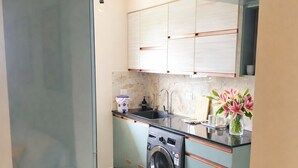 A compact kitchen with a washing machine, a sink, and a countertop with a vase of flowers.