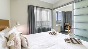 A hotel room with a bed, a desk, a chair, a window with curtains, and a view of the city. - Living the Dream on Level 18! (Darwin City)
