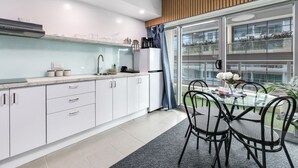 Une cuisine moderne avec des meubles blancs, un plan de travail en marbre et un coin repas comprenant une table en verre et des chaises noires.