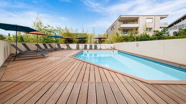 A rooftop pool with wooden decking, lounge chairs, and umbrellas. - Flat with a balcony offering views of the mountains and the swimming pool (Grasse)