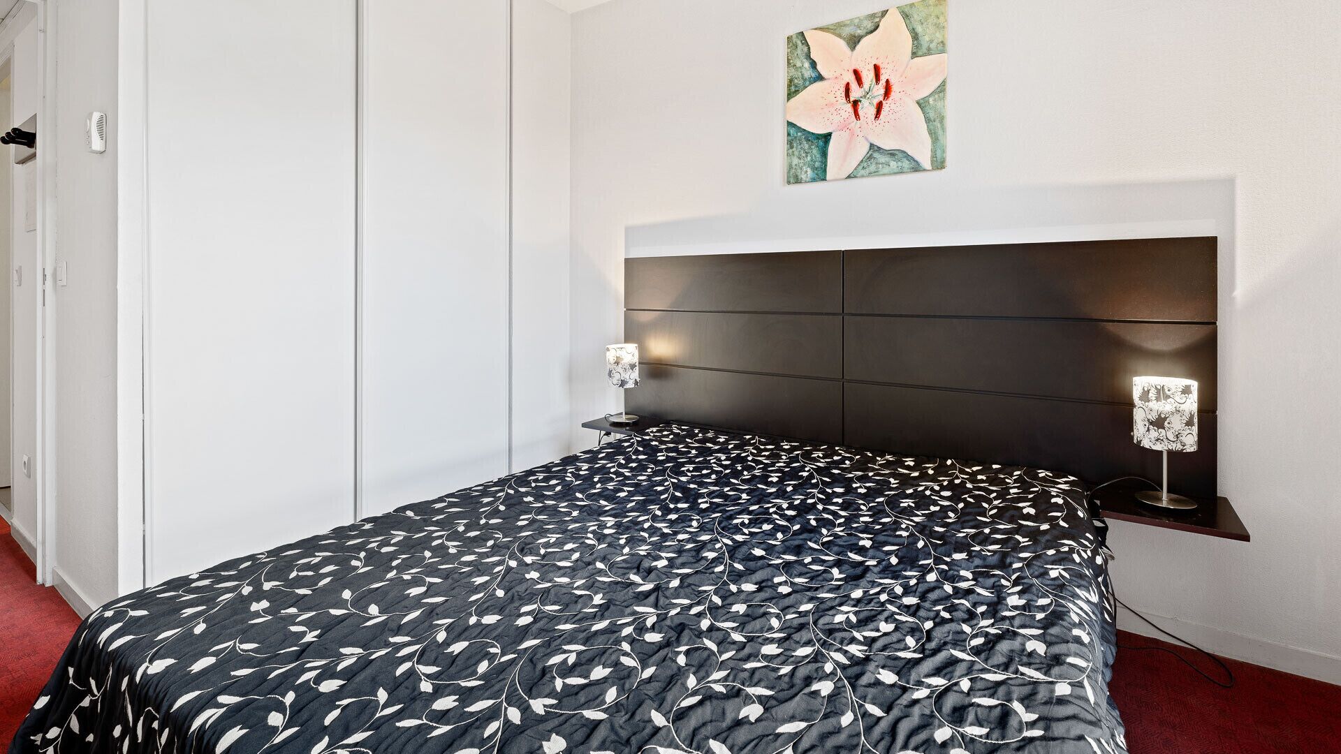 A bedroom with a bed, a headboard, bedside lamps, and a wall-mounted artwork.