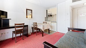 A compact room with a bed, a desk with a television, a dining table with chairs, a kitchenette, and a wardrobe. - Flat with a balcony offering views of the mountains and the swimming pool (Grasse)