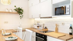 Una cocina moderna con armarios blancos, microondas integrado, cafetera y encimera de madera.