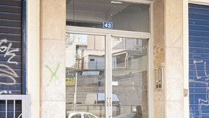 La entrada de un edificio con puerta de vidrio, el número '43' arriba y una persiana azul a la derecha.