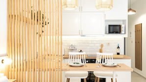 Una cocina moderna con armarios blancos, un microondas, una mesa de comedor de madera con sillas blancas y dos lámparas colgantes.