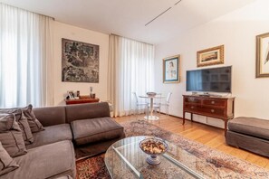 Ein Wohnzimmer mit einer Couch, einem Glastisch, einem Fernseher, einem kleinen Tisch mit Stühlen und Kunstwerken an den Wänden.