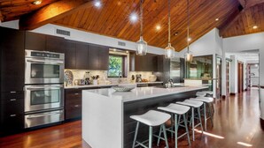 Cozinha moderna com eletrodomésticos de aço inoxidável, uma ilha grande com banquetas e vigas de madeira no teto.