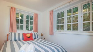 A bedroom with a bed, two windows, a bedside table, and a lamp. - Lost In The Woods Lodge (Bodmin)