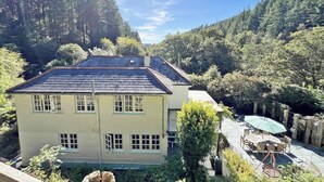 A two-story building with a sloped roof, surrounded by dense forest. - Lost In The Woods Lodge (Bodmin)