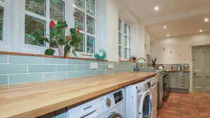 A modern kitchen with a washing machine, a sink, and a window with a view of greenery. - Lost In The Woods Lodge (Bodmin)