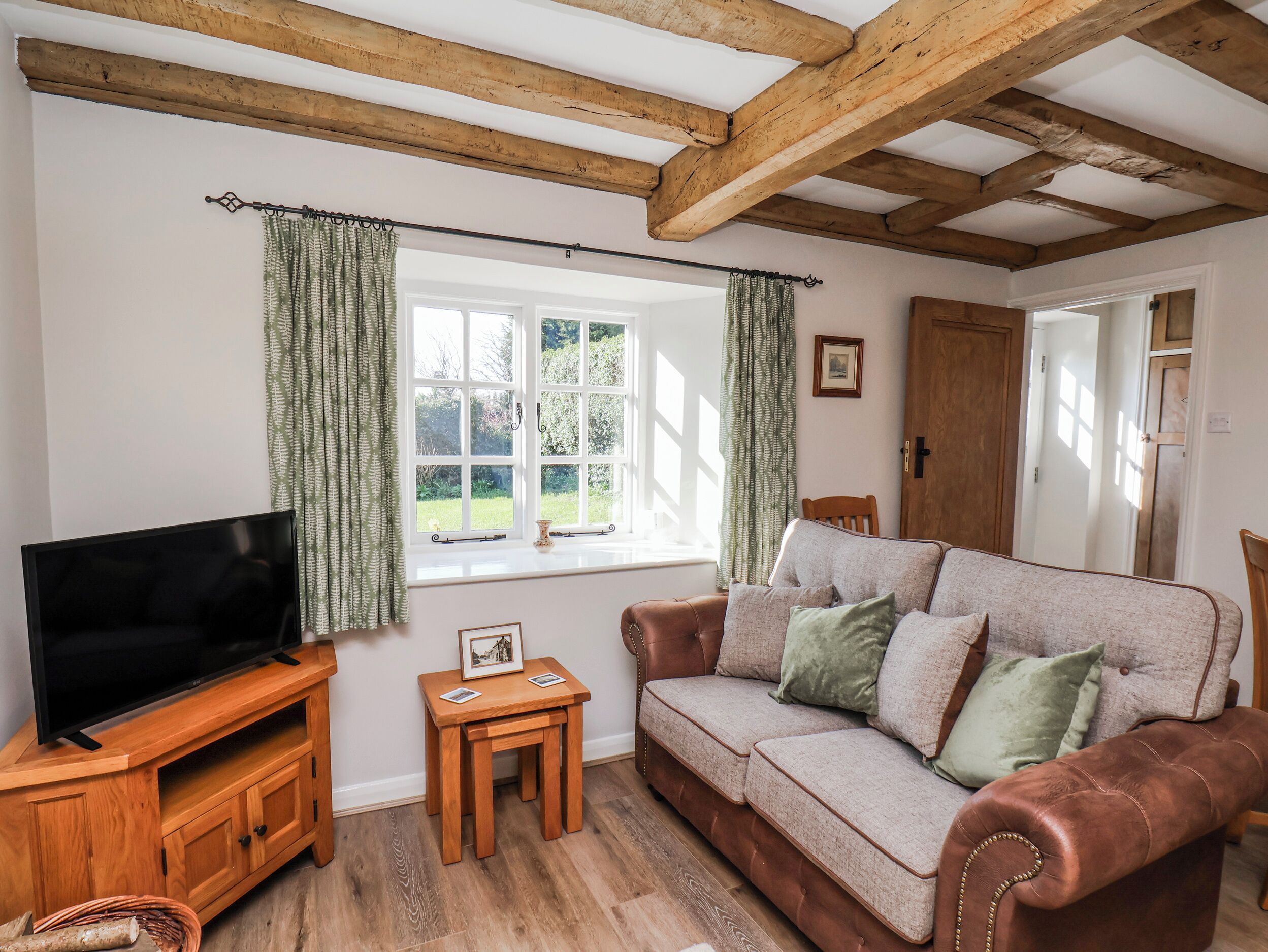 A cozy living room with a wooden TV stand, a sofa, a small table, and a window with curtains.