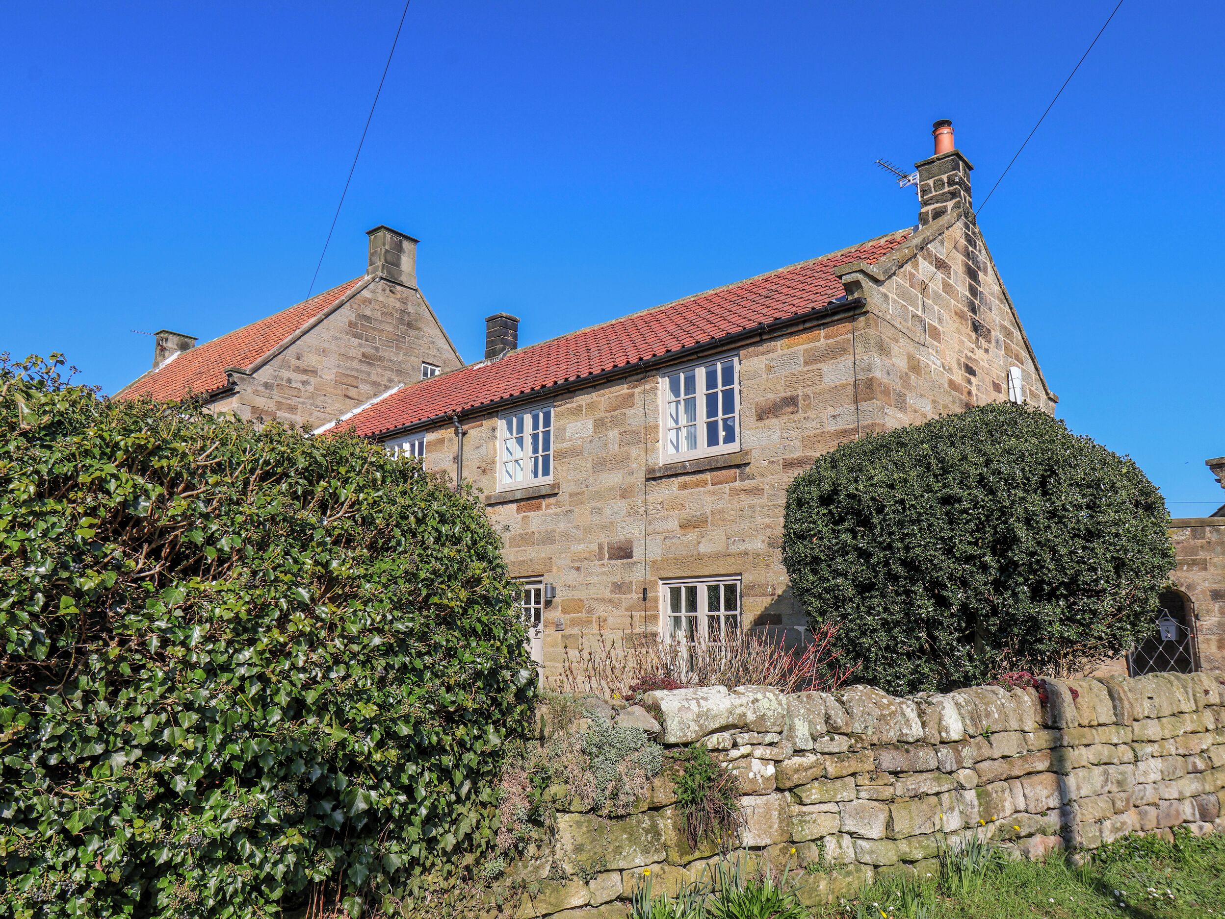 A stone building with a red-tiled roof, stone walls, and a stone wall in the foreground.
