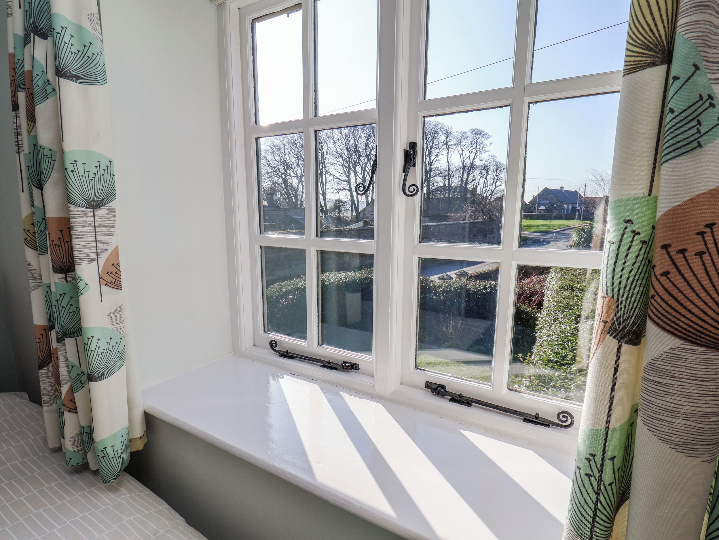 Quarto com uma grande janela, um banco branco e cortinas estampadas.