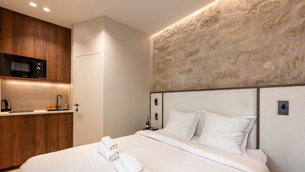 A hotel room with a bed, a wooden kitchenette, and a stone wall. - Designer Studio steps from Lafayette (Paris)