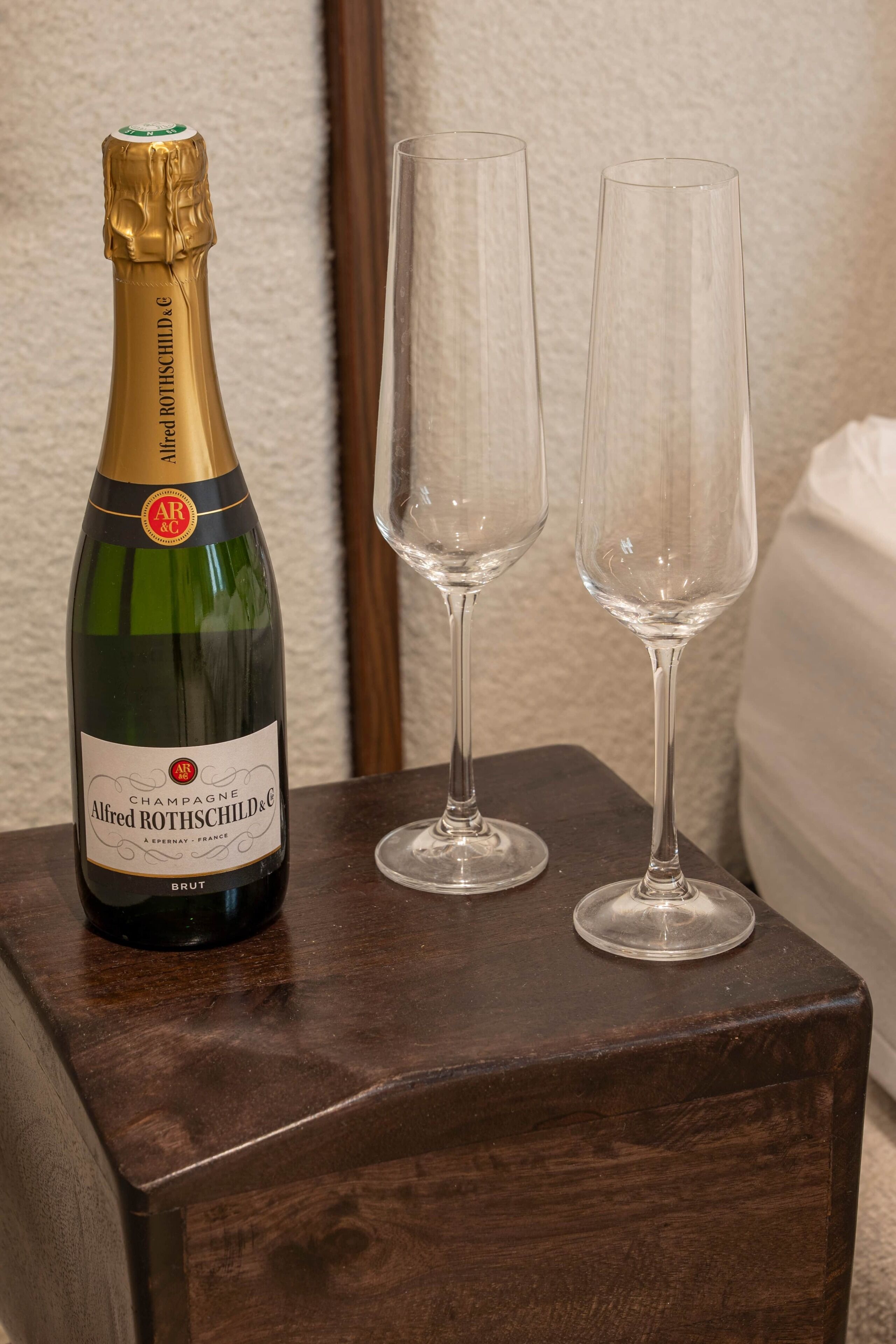 A bottle of Alfred Rothschild champagne and two empty glasses on a wooden table.