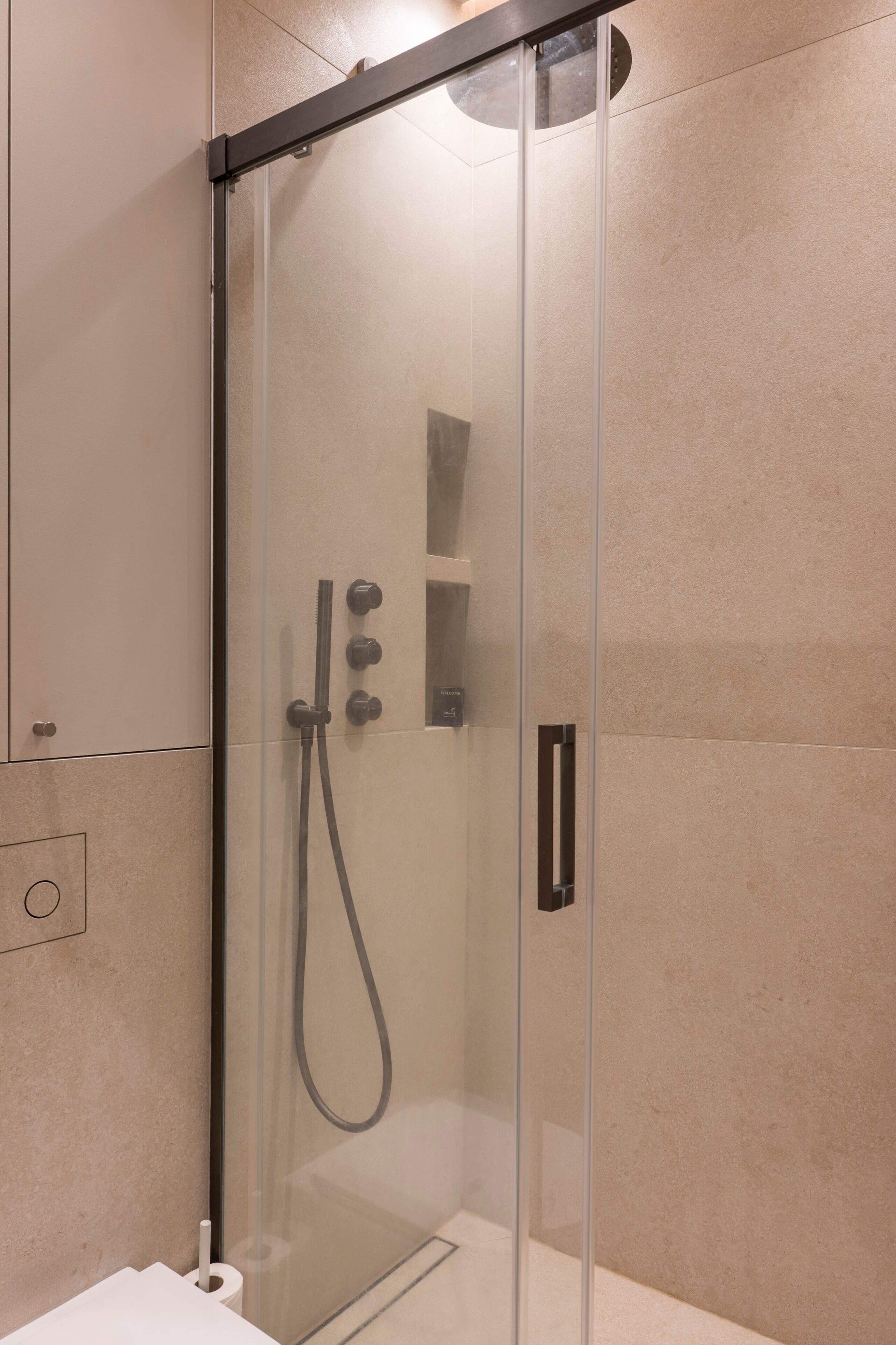 A modern shower enclosure with a glass door, a handheld showerhead, and a wall-mounted control panel.