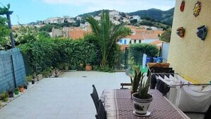 Eine Terrasse im Freien mit Tisch, Stühlen, einem Blumentopf und Blick auf eine Hügelstadt.