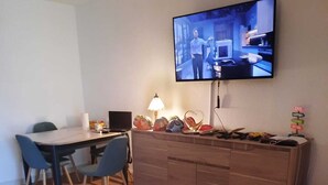 Eine moderne Küche mit Fernseher, Holzschränken, einem Esstisch mit Stühlen und einer Lampe.
