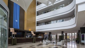 A modern hotel lobby with a central reception desk, multiple seating areas, and a multi-level atrium.