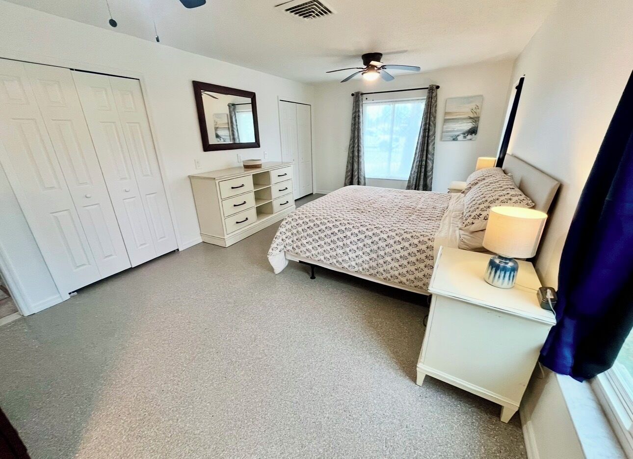 A bedroom with a bed, a nightstand, a dresser, a ceiling fan, and a window with curtains.