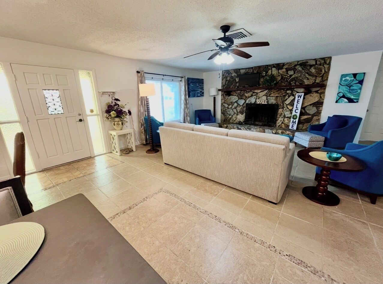 A living room with a sofa, a dining table, a ceiling fan, and a stone fireplace.