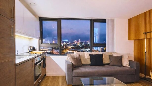 Een moderne woonkamer met een bank, een glazen salontafel en een uitzicht op een stadsgezicht door grote ramen.