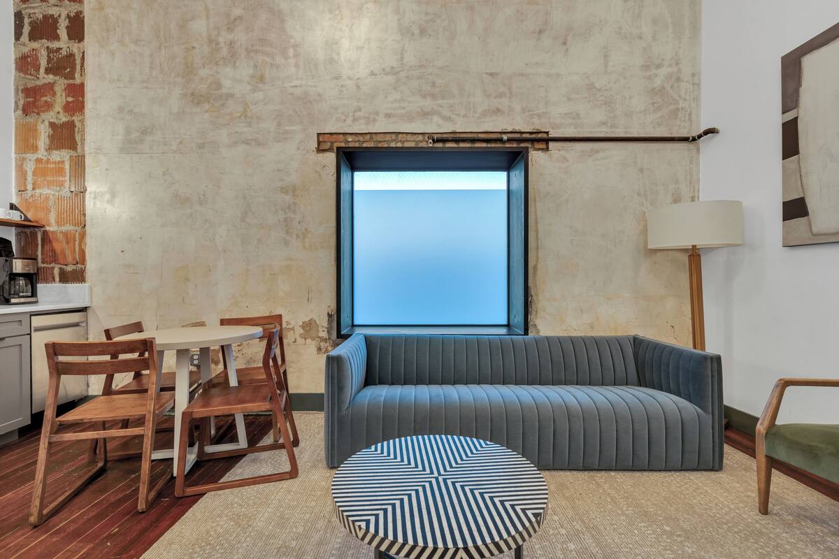A room with a sofa, a round table, a lamp, and a window.
