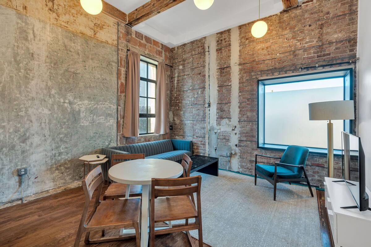 A room with exposed brick walls, a round table with chairs, a sofa, a television, and a lamp.