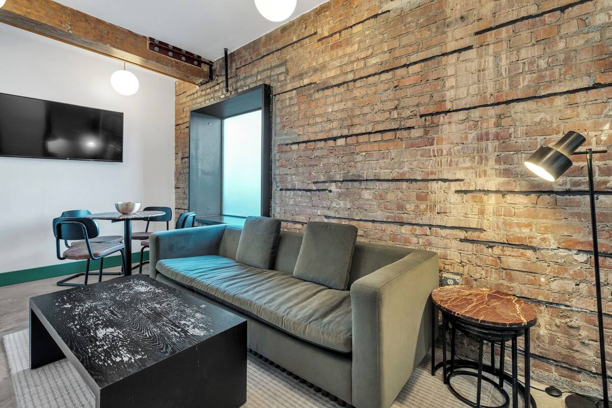 A modern living room with a brick wall, a sofa, a coffee table, a TV, and a lamp.