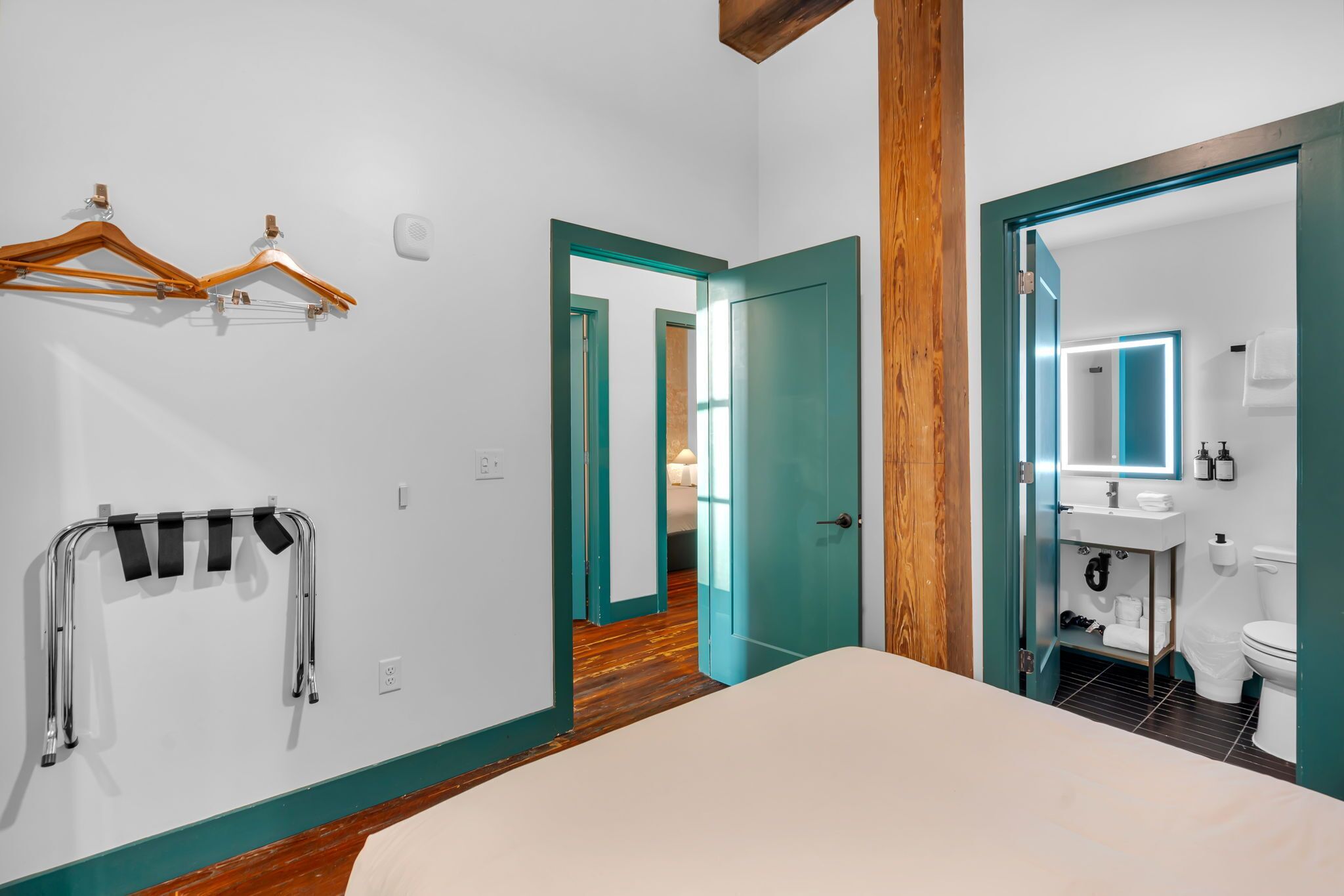 Una camera da letto con un letto, pavimento in legno, una porta verde acqua e un bagno con specchio e lavandino.